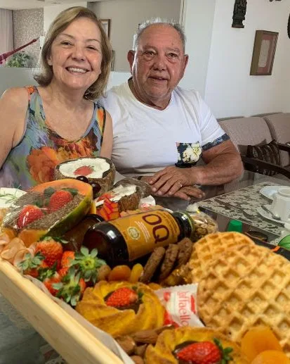 Casal de idosos, sorrindo e felizes, por receber uma linda Bandeja de café da manhã Premium, para comemorar seu aniversario de casamento.